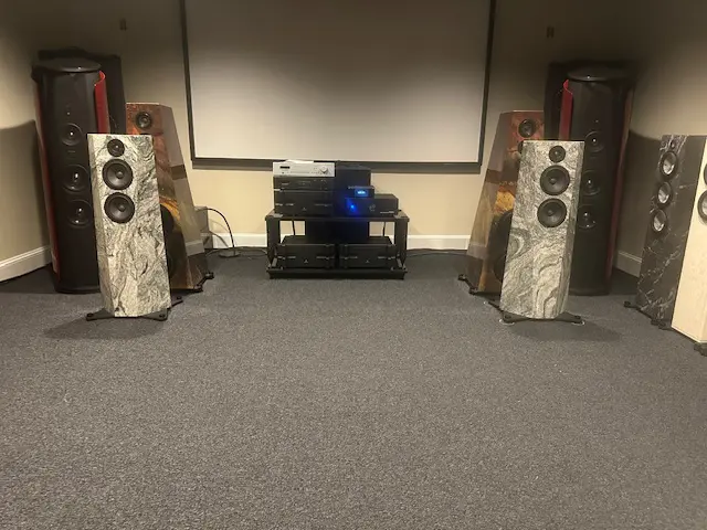 High-end audio setup with large speakers and a projector screen in a cozy room.
