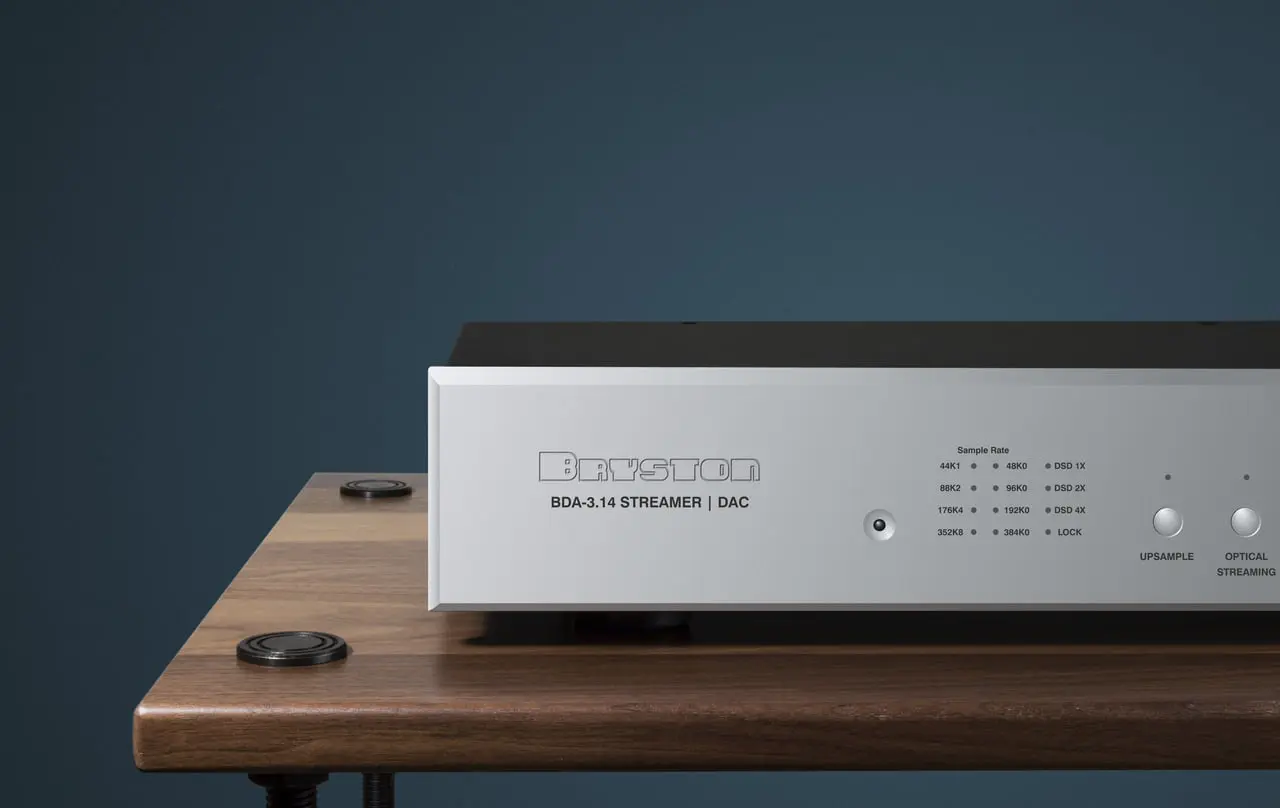 A sleek audio amplifier on a wooden table against a dark background.