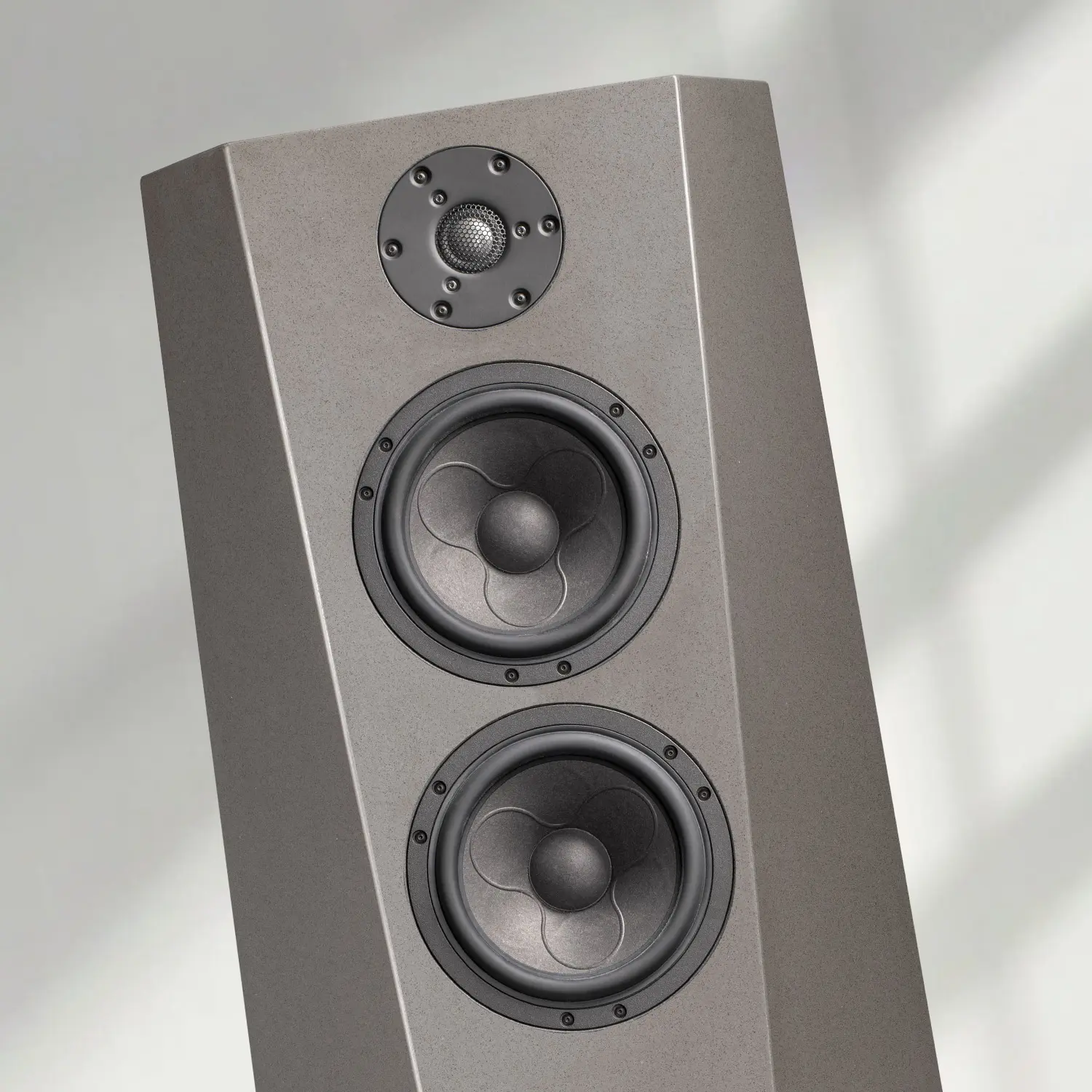 A modern gray speaker with three drivers against a light background.