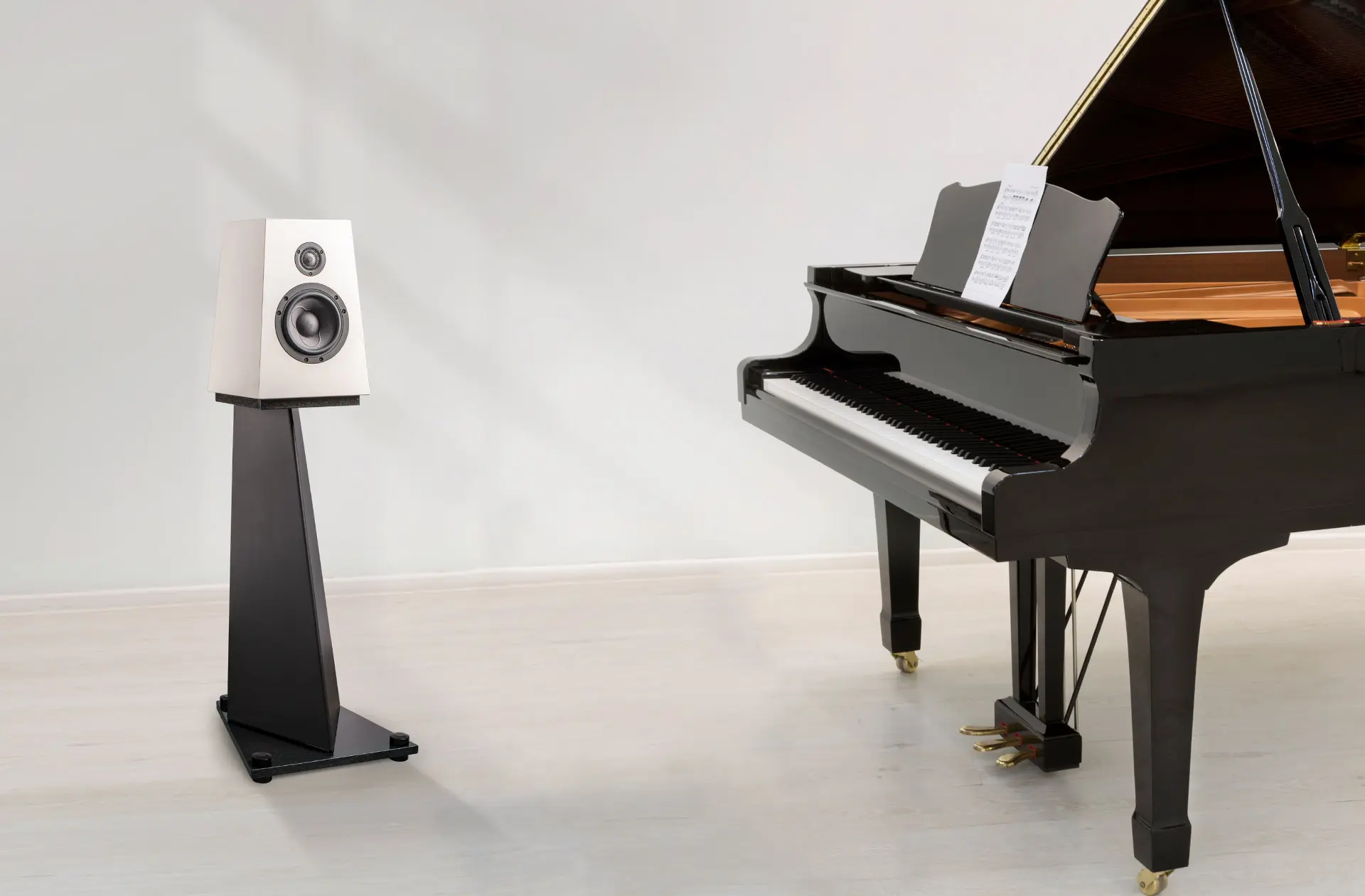Modern speaker on a stand beside a grand piano with sheet music.