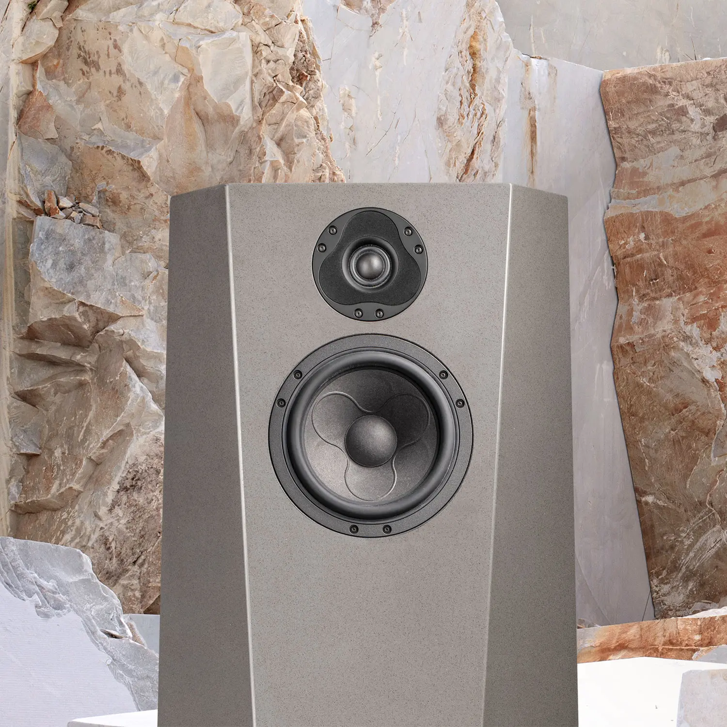 Modern gray speaker against a textured stone wall.