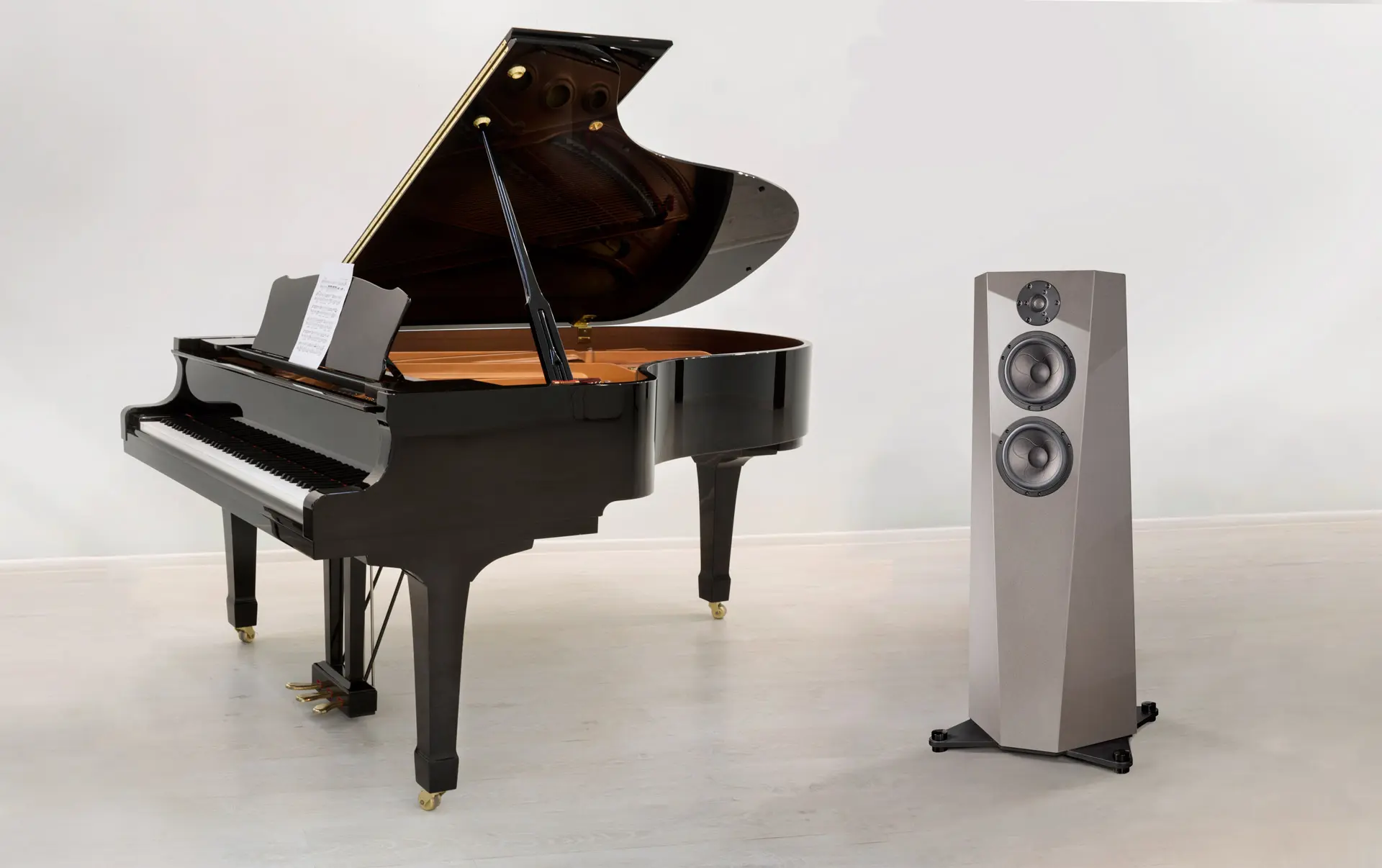 Black grand piano and modern speaker on white floor and wall.