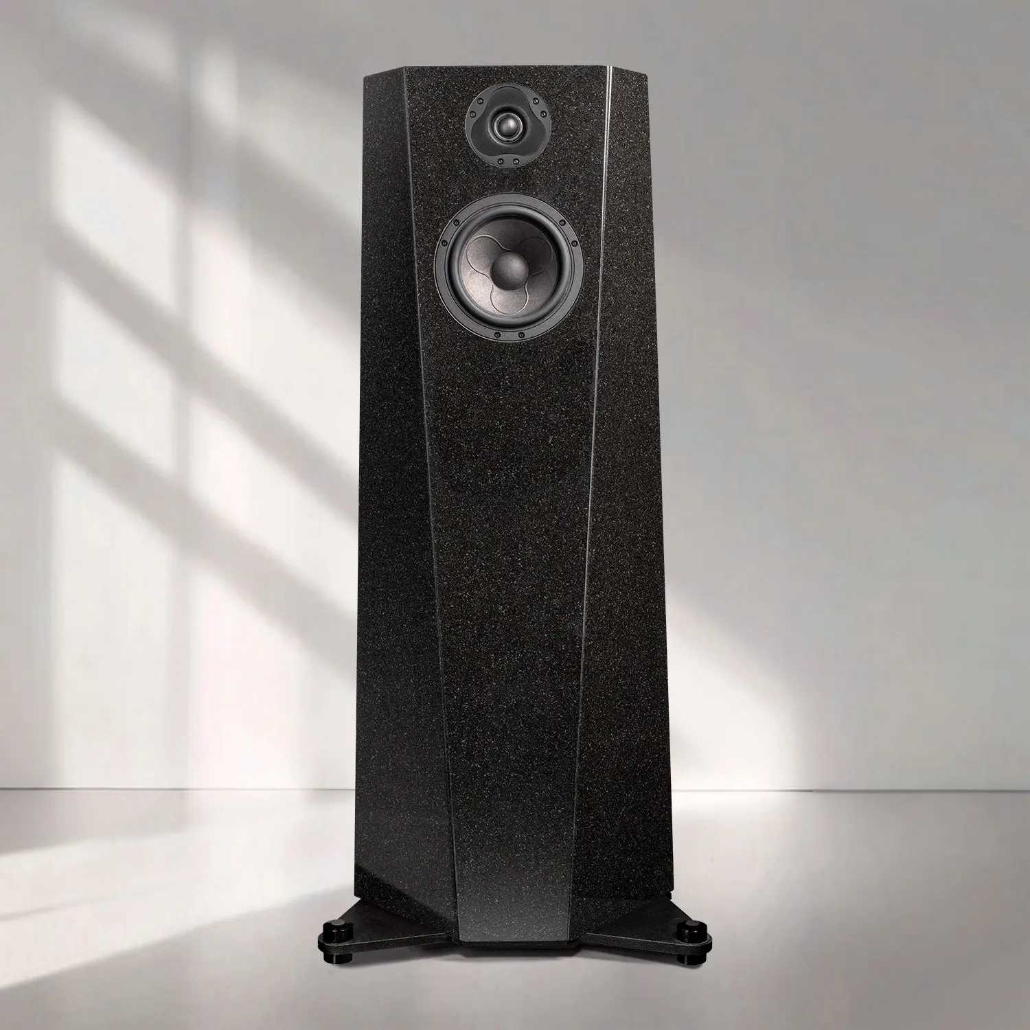 A sleek black floor-standing speaker with sunlight casting shadows behind it.