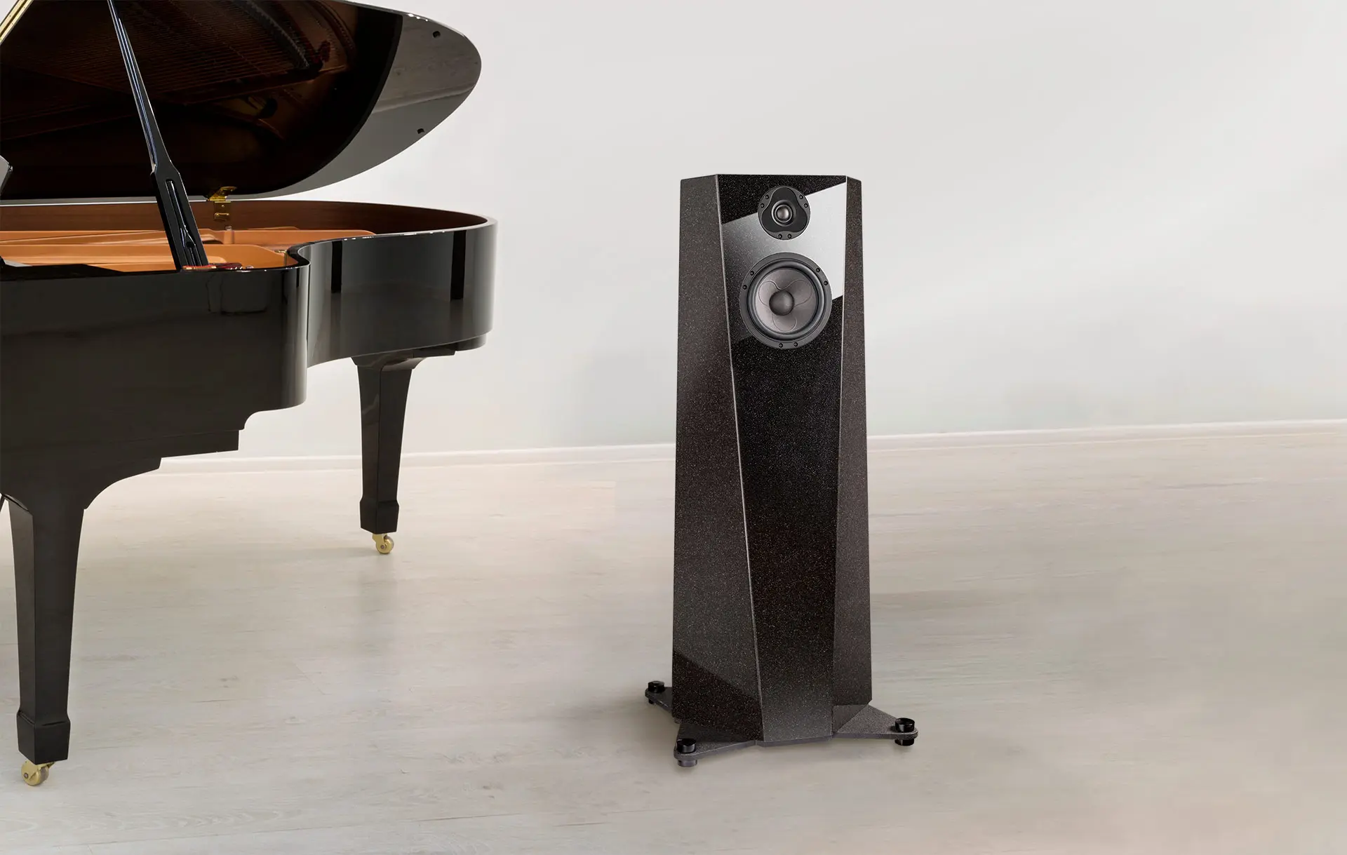 A sleek black floor-standing speaker beside a grand piano leg.