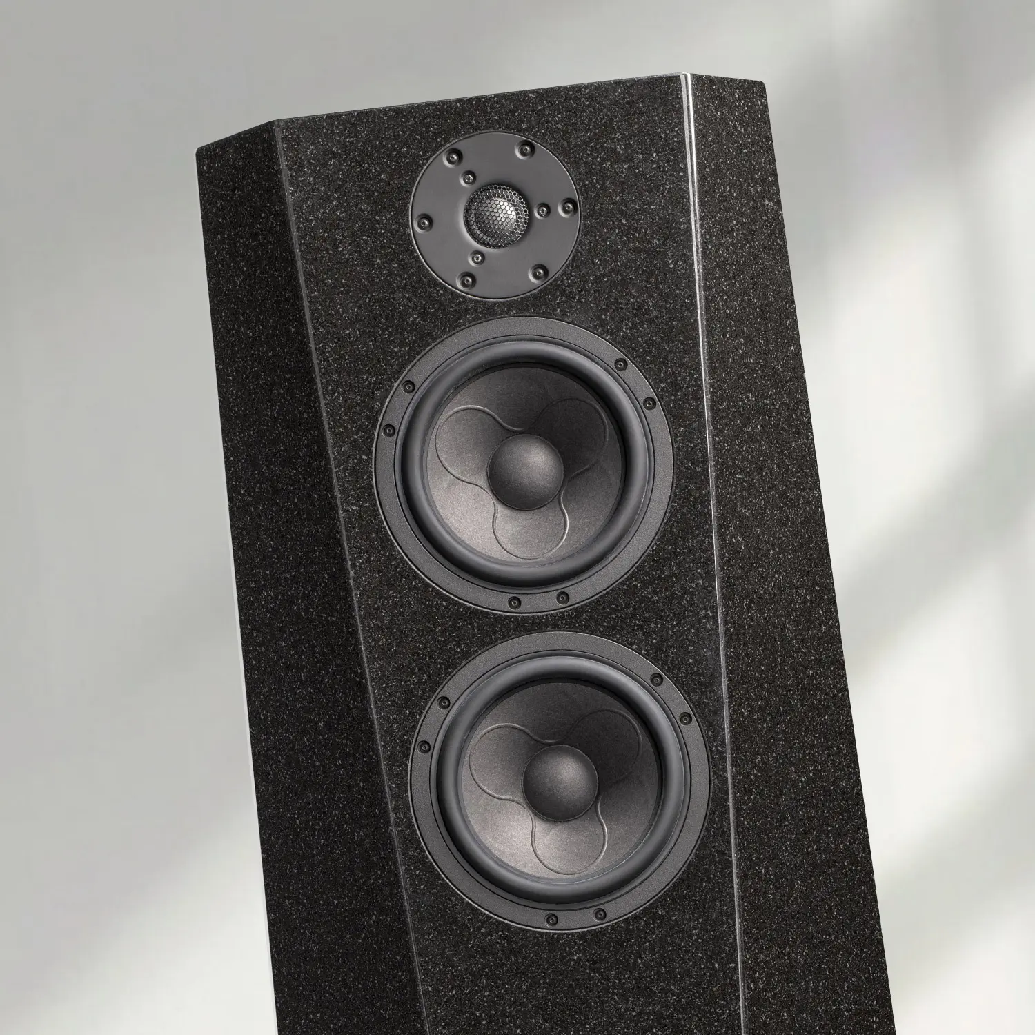 A sleek black tower speaker with three drivers in a softly lit room.