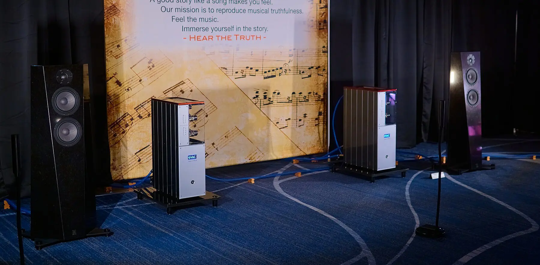 Two large speaker systems set up in a room with a music-themed wall.