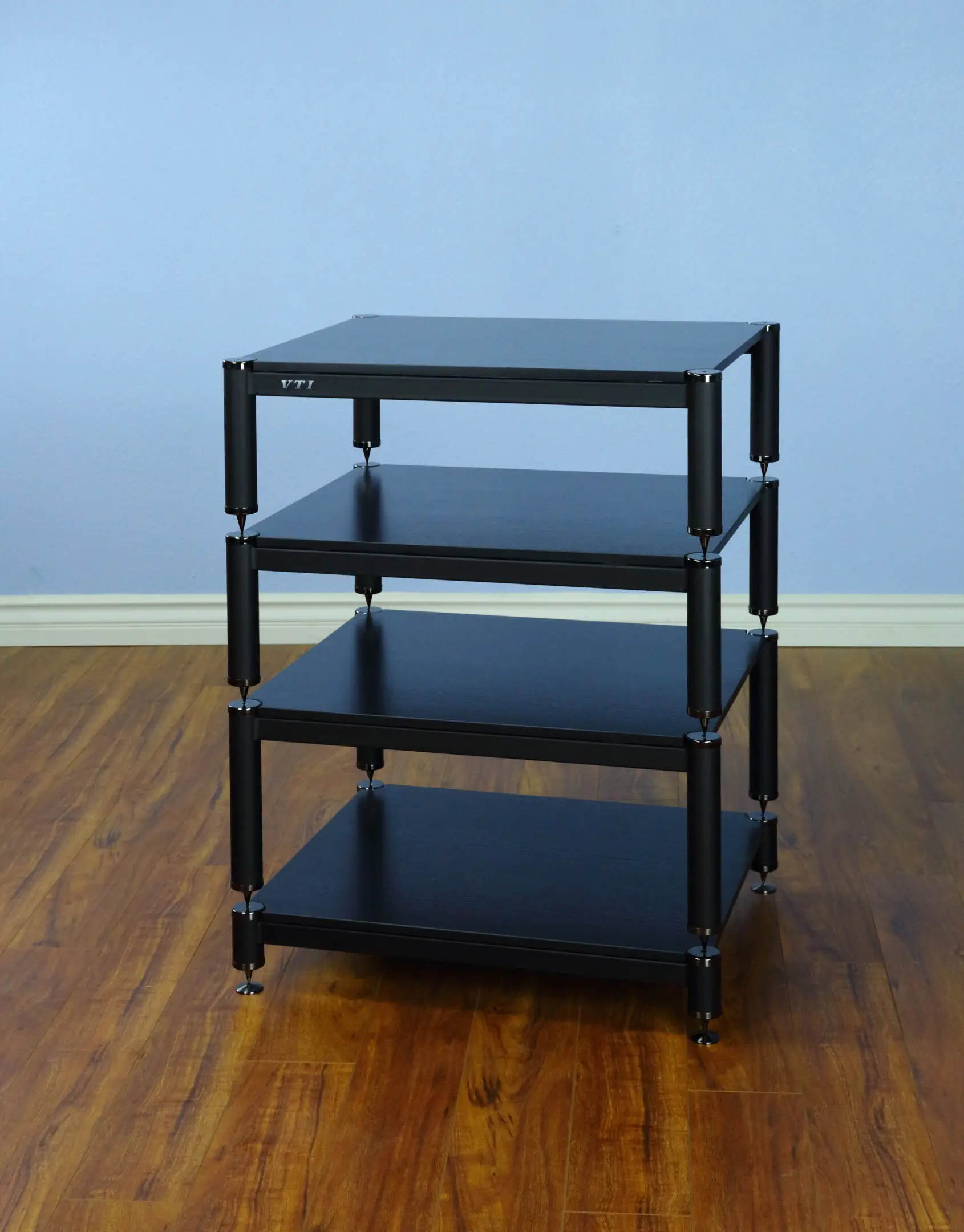 A black four-tier rolling utility cart with shelves on a wooden floor.