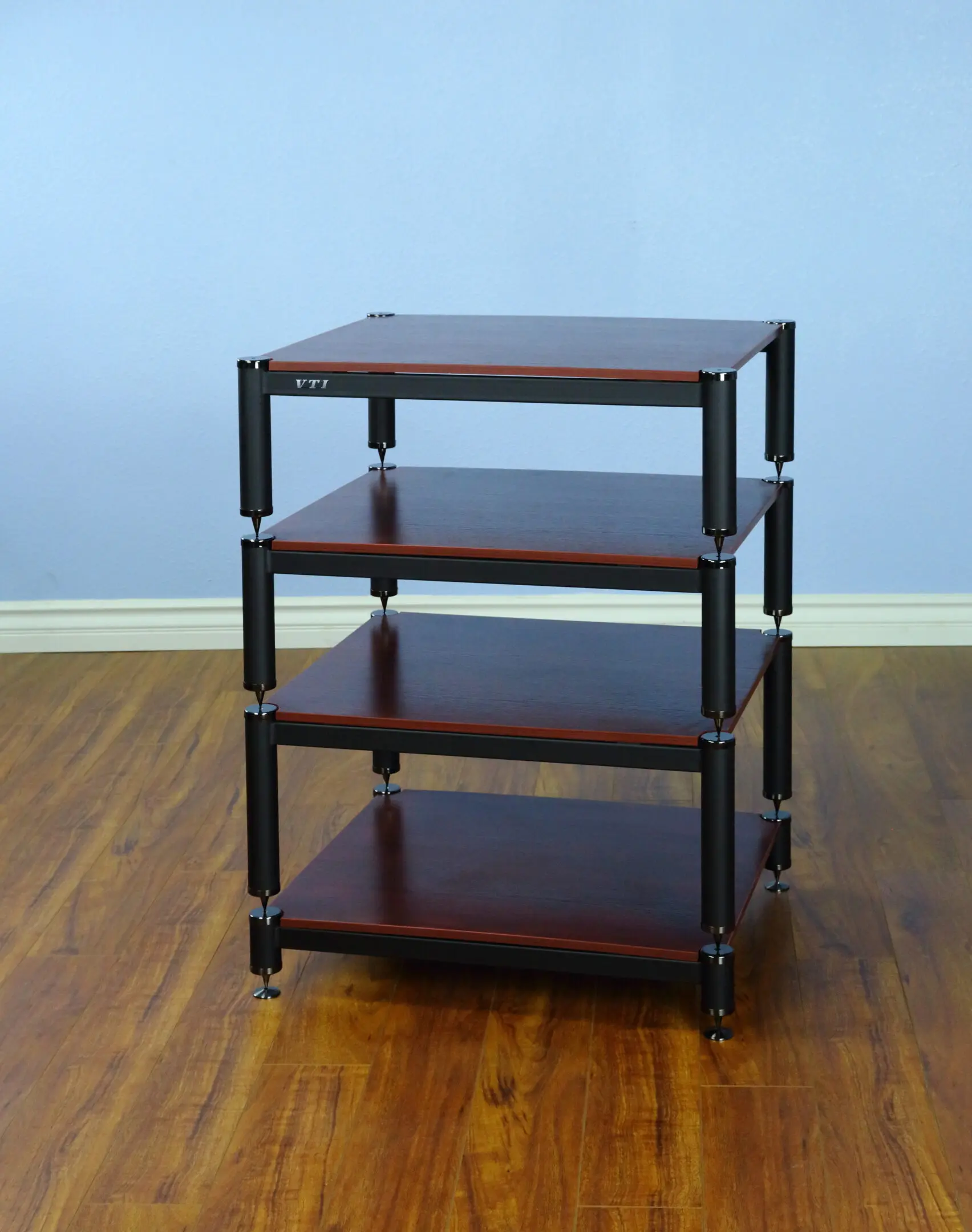A dark wooden four-tier shelving unit with turned legs against a light blue wall.
