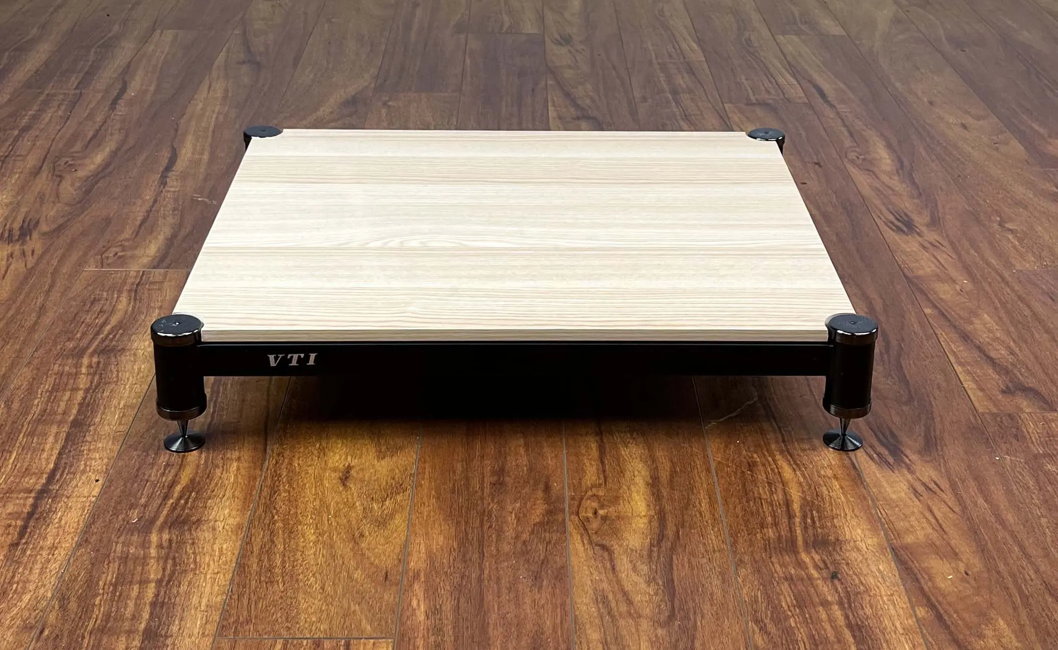 A wooden lap desk with black metal legs on a wooden floor.