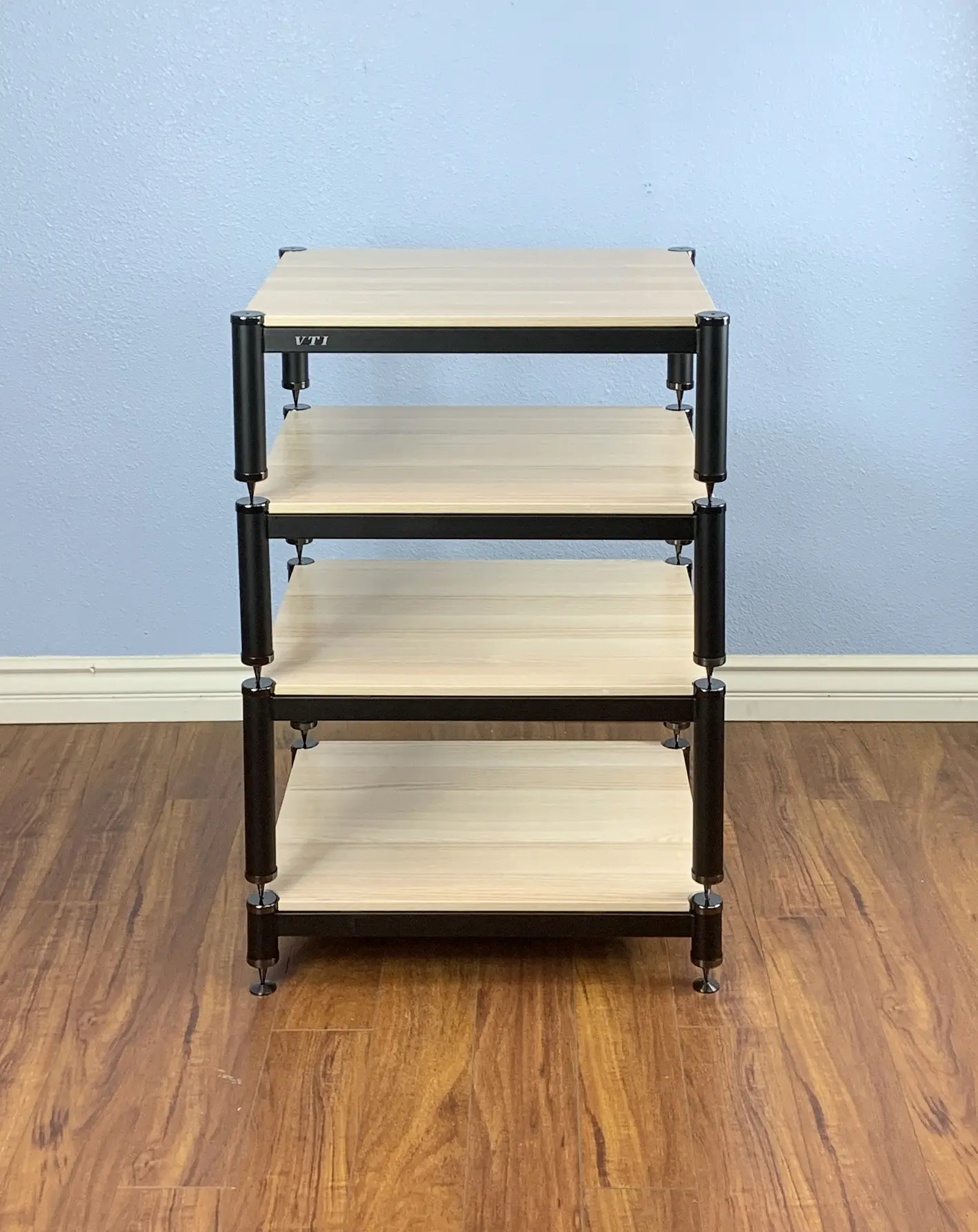 A four-tier wooden and metal shelf unit against a blue wall.