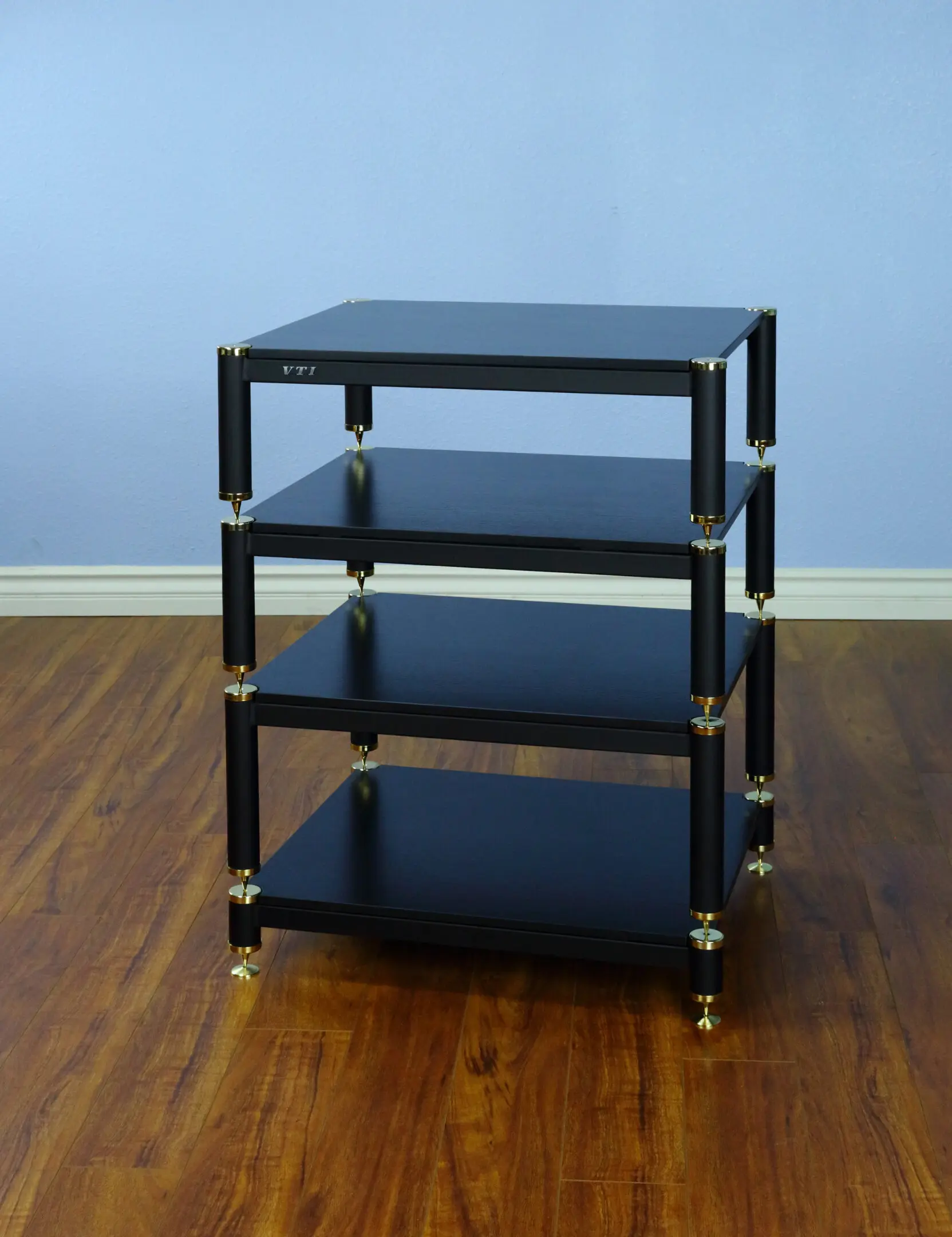 A black four-tier audio rack with metal supports on wooden floor.