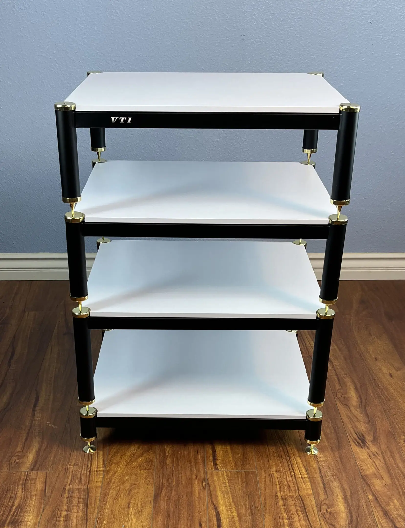 A four-tier black and white rolling utility cart on a wooden floor.