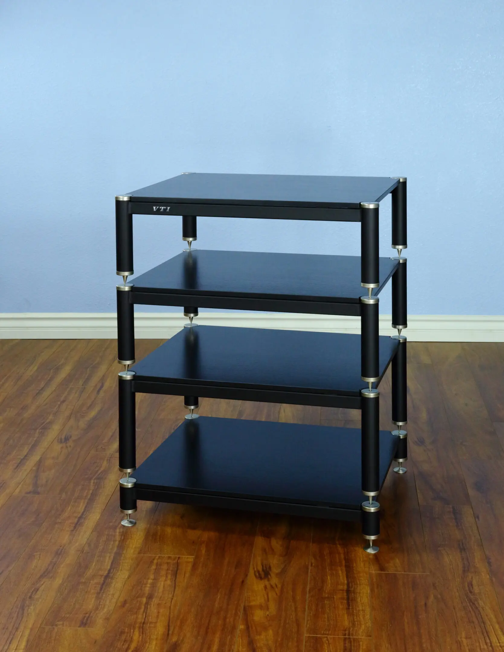 A black four-tier shelving unit on wheels against a blue wall.
