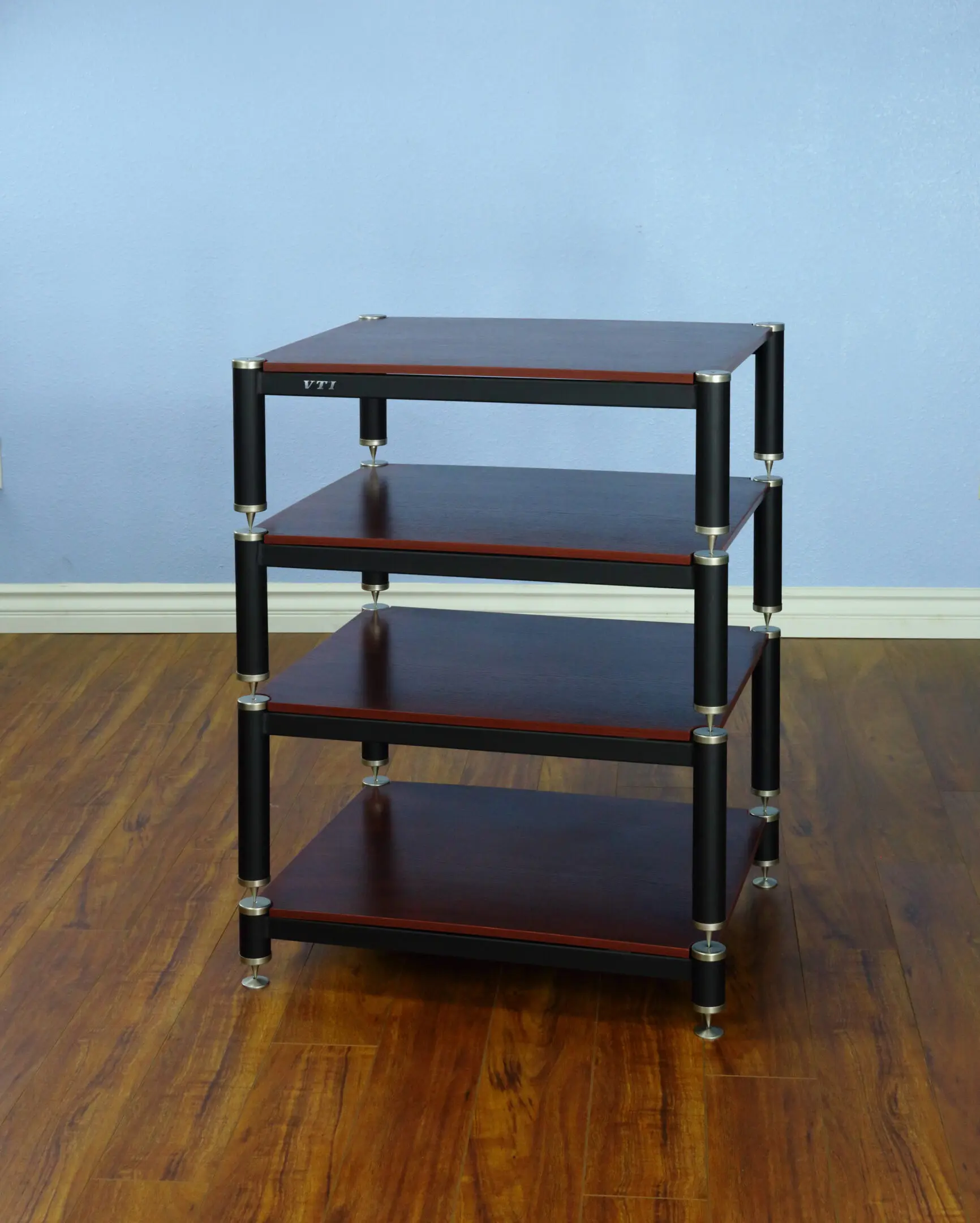 A four-tier wooden and metal shelving unit on wheels against a blue wall.