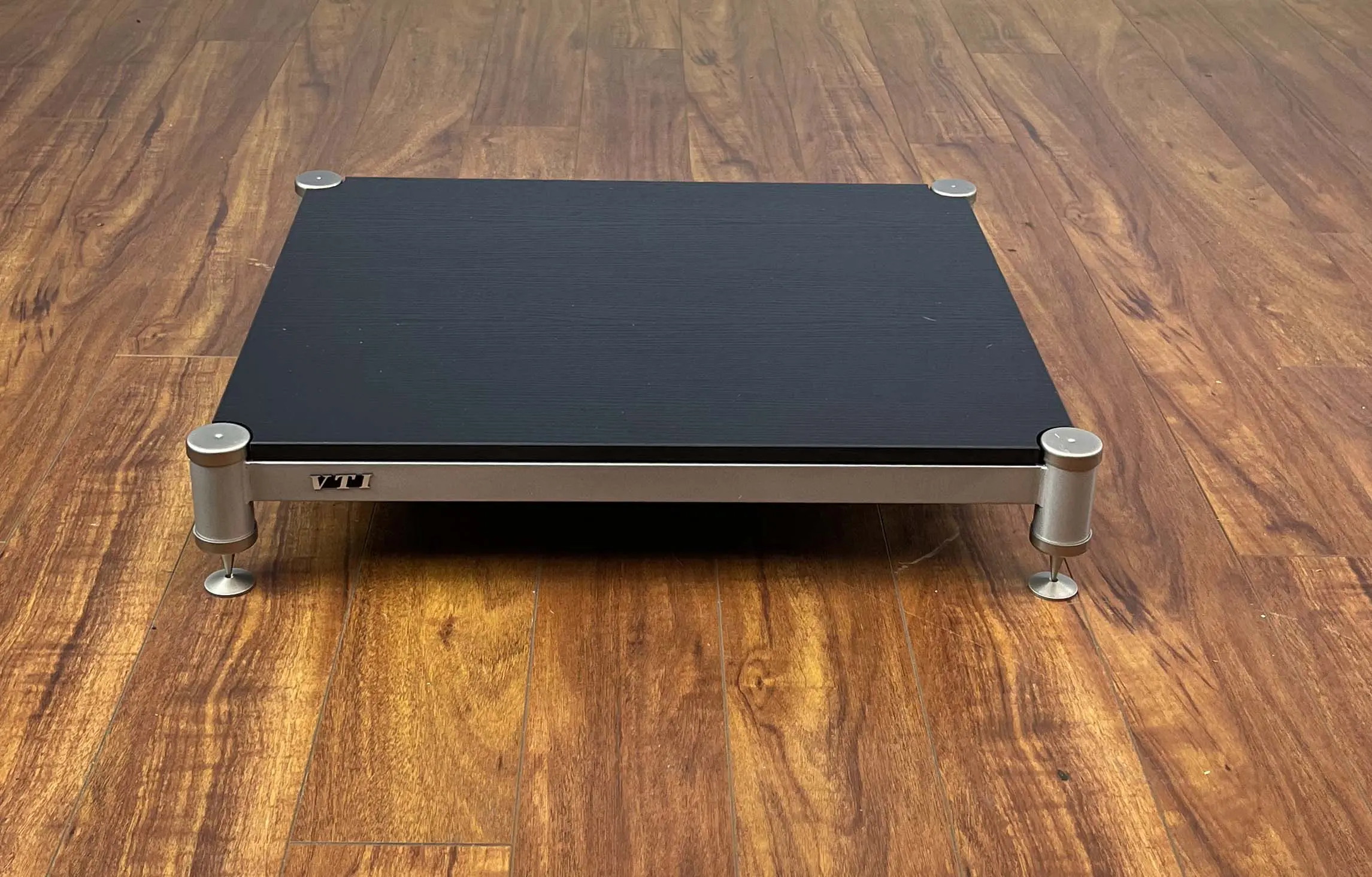 Black laptop cooling pad with adjustable metal legs on wooden floor.