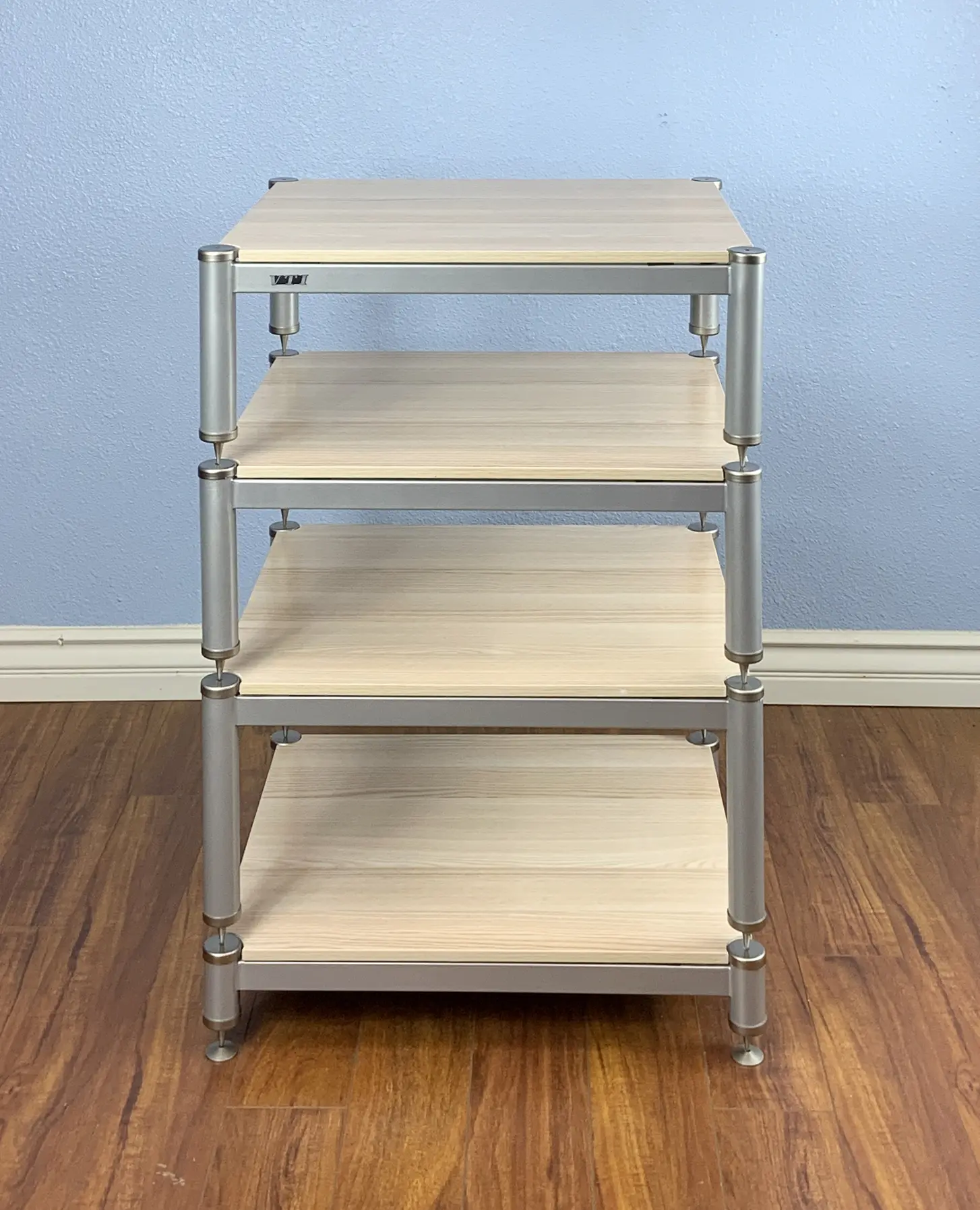 A four-tier wooden shelf with metal frame on a wooden floor.