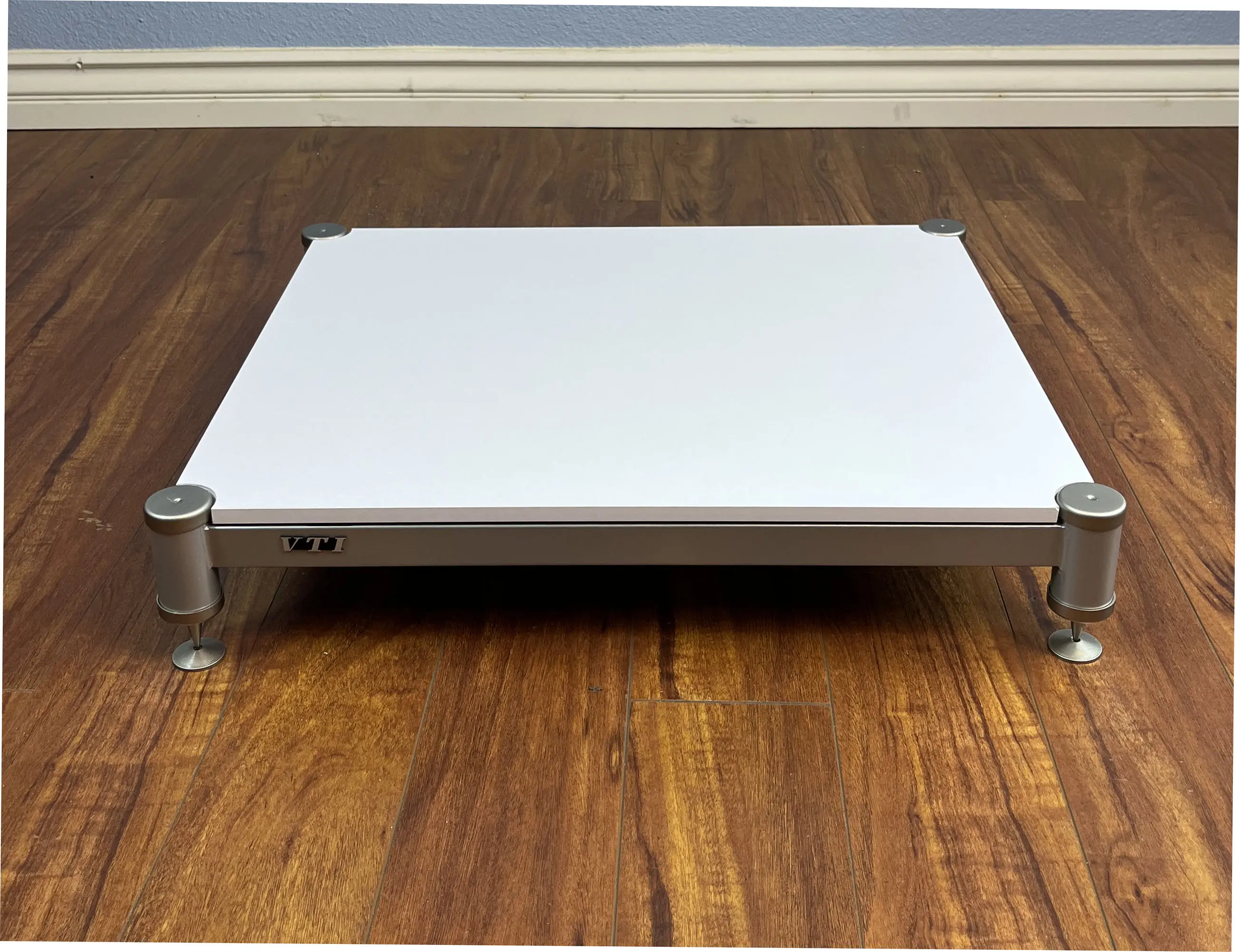 A sleek, modern white platform with metallic legs on a wooden floor.
