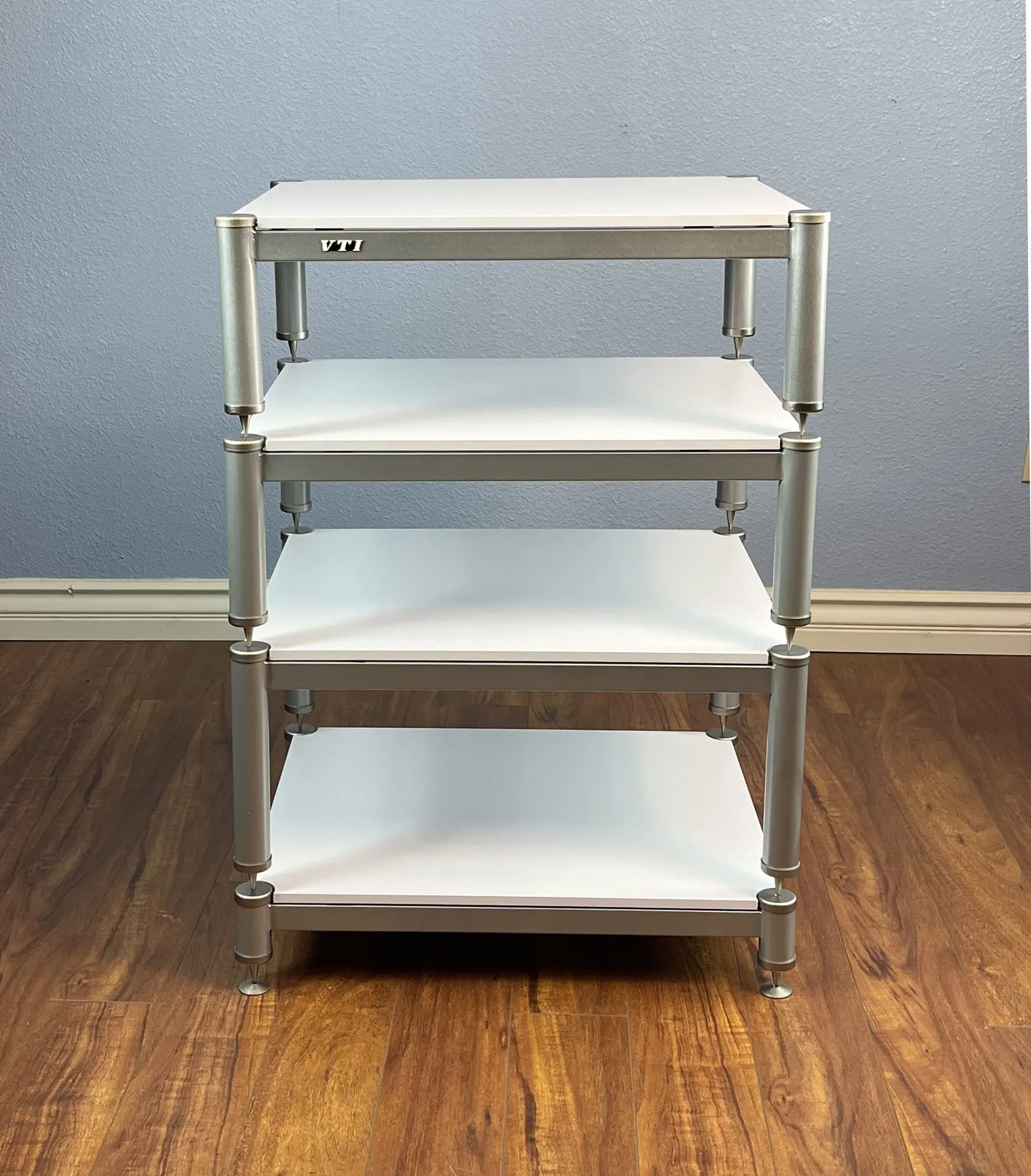 A four-tier white shelving unit with metal frame on wooden floor.