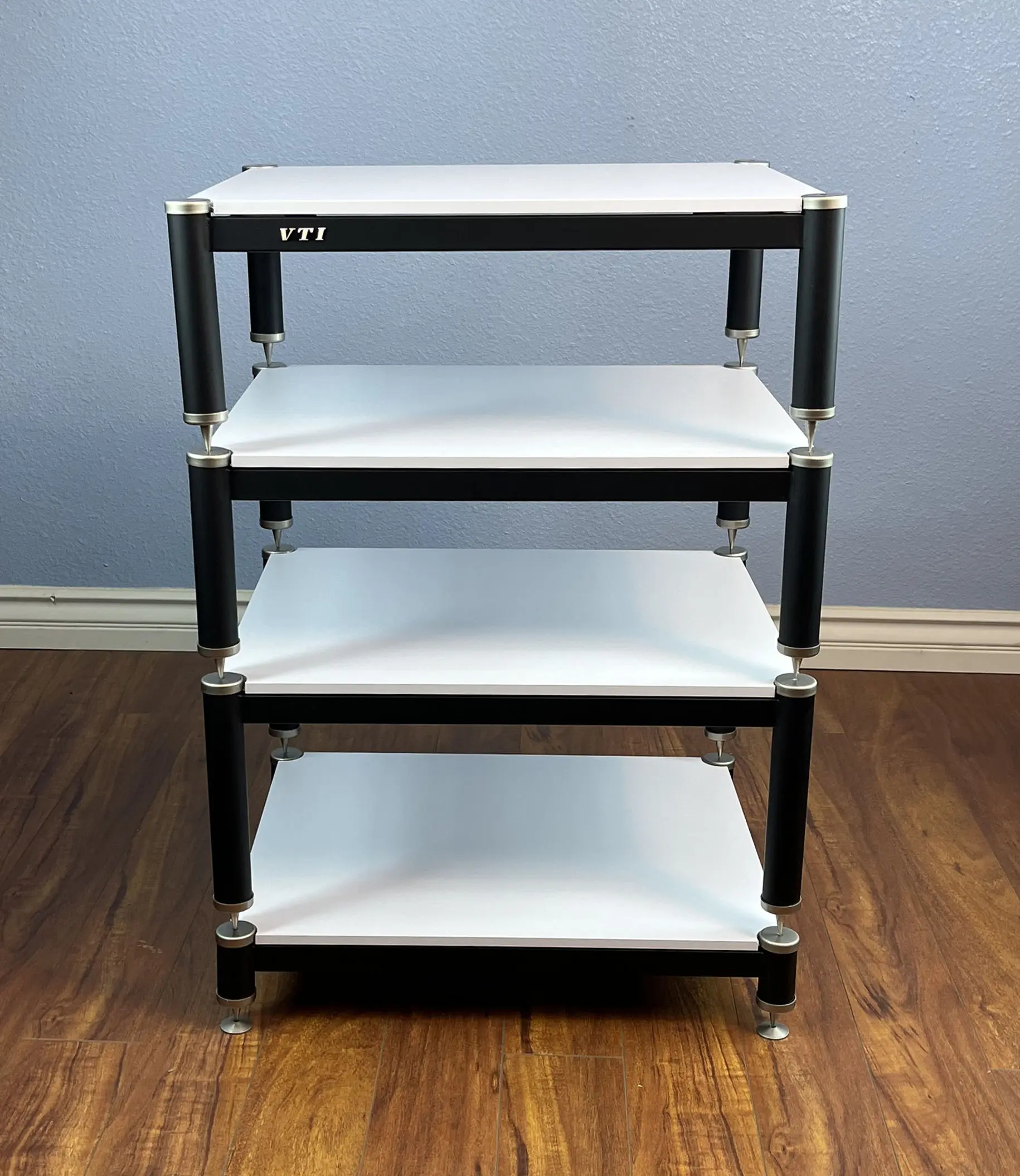 A four-tier black and white utility cart with wheels on hardwood floor.
