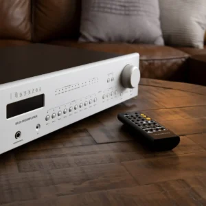 A white audio receiver and remote on a wooden table in a cozy living room.