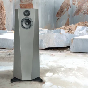 Modern gray speaker standing on a rocky surface outdoors.