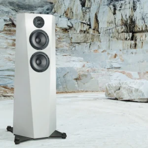 Modern white floor-standing speaker in a rocky outdoor setting.