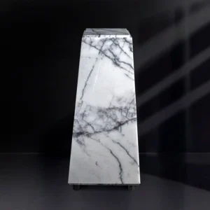 A sleek, white marble obelisk with gray veining against a dark background.